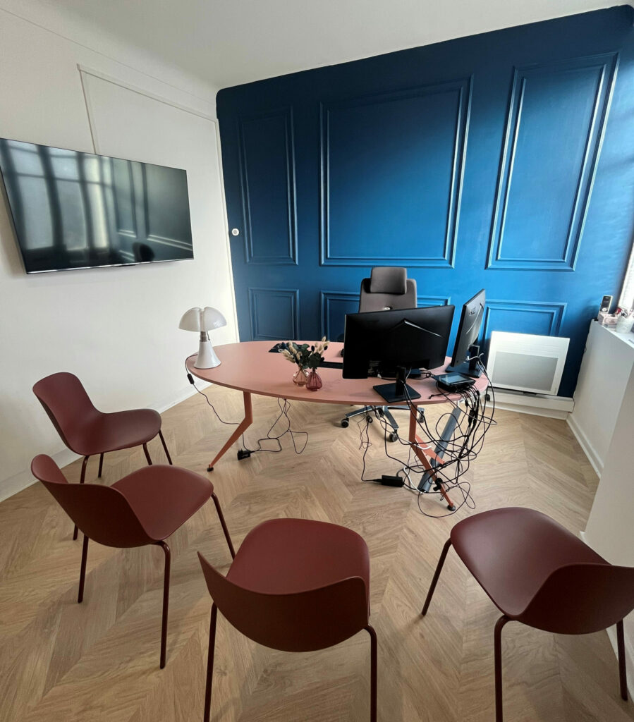 Bureau moderne et épuré du notaire-marie-tayac à Mont-de-Marsan, avec écran, chaises rouges et mur bleu